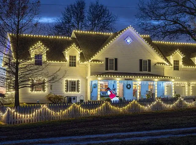 A Cape Cod roofline with lit bushes below