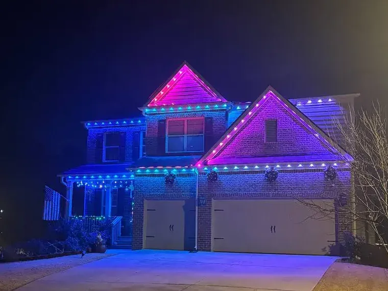 Close view of a two-story roofline lit pink and blue by a permanent LED track