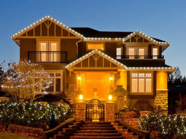 A Craftsman roofline over lit hedges