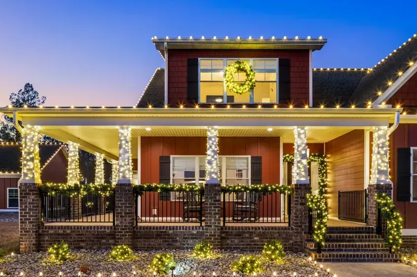 House with lights along the porch rail and the roofline at night